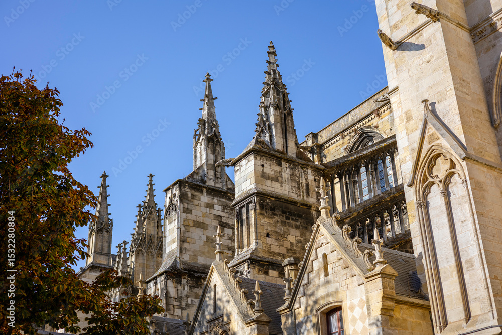 Fototapeta premium Close up of the exterior walls of Bordeaux Cathedral, featuring Gothic architectural details such as windows, pointed arches, pinnacles, and gargoyles under a blue sky. Bordeaux, Gironde, France.