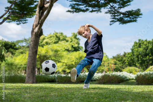 Little boy playing football in the garden with morning sunrise