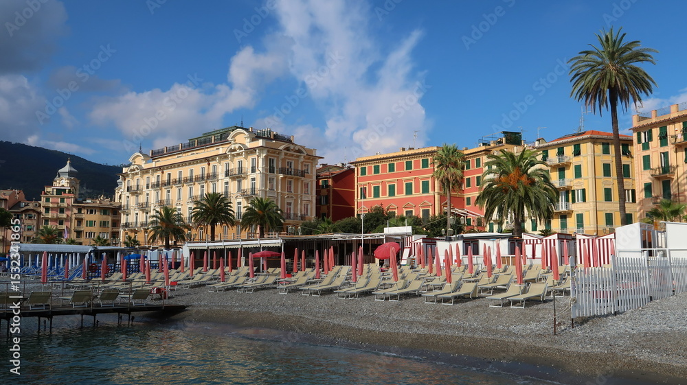 Obraz premium Plage privée et immeubles colorés dans la ville de Santa Margherita Ligure en Ligurie, sur la Riviera italienne, avec des transats, des parasols et des palmiers au bord de la mer Méditerranée (Italie)