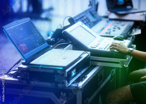 Close-up of a sound engineer operating a lighting or audio console and laptop during a live event. Professional event production and stage control setup with modern digital equipment.