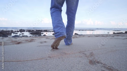 Cinematic gimbal shot of a man walking on a rocky beach during sunset, captured from behind. Soft pastel skies, calm waves, and solitude make this perfect for emotional or travel storytelling.