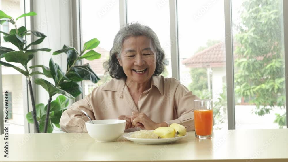 Healthy elderly Asian woman sits down to eat lunch with meatless, easily digestible congee and a banana and freshly squeezed orange juice rich in vitamin C with satisfaction. Healthy elderly Asian woman sits down to eat lunch with meatless, easily digestible congee and a banana and freshly squeezed orange juice rich in vitamin C with satisfaction.