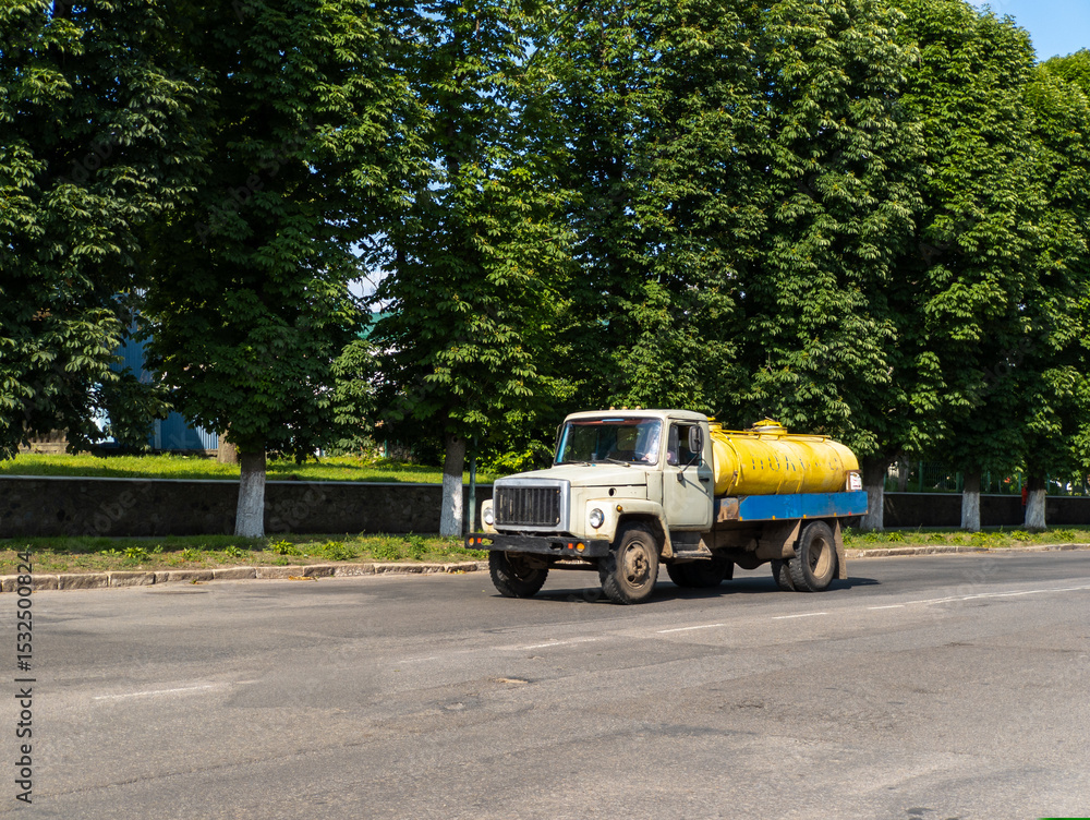 Obraz premium A yellow and blue truck driving down a street next to trees