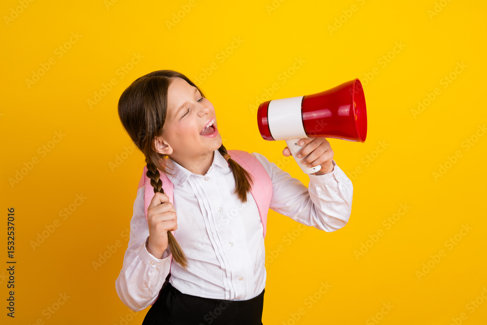 Cheerful schoolgirl with a megaphone expressing excitement wearing a white shirt against a vibrant yellow background Cheerful schoolgirl with a megaphone expressing excitement wearing a white shirt against a vibrant yellow background