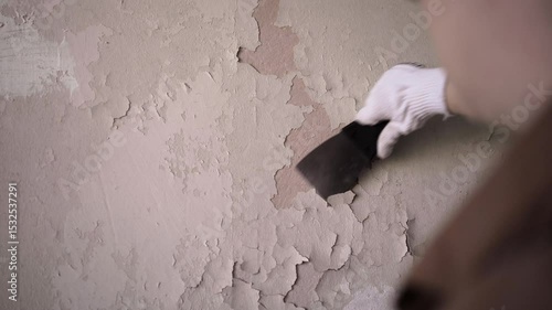 Female builder or repair worker removing old painted from wall. House renovation and renewal