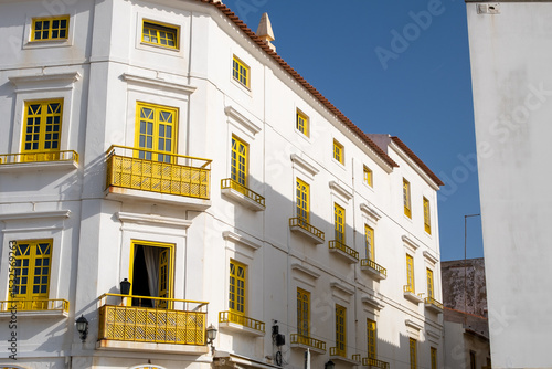 Side view of white building with yellow framed windows and balconies under sunny blue sky. Urban street scene in Portugal.