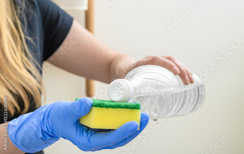 The cleaning lady holds a cleaning sponge in her hand and a bottle of spirit vinegar