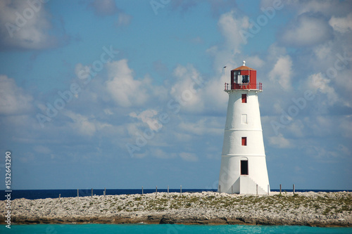 A white lighthouse with a red top stands on a rocky point, overlooking the turquoise waters near Nassau, Bahamas