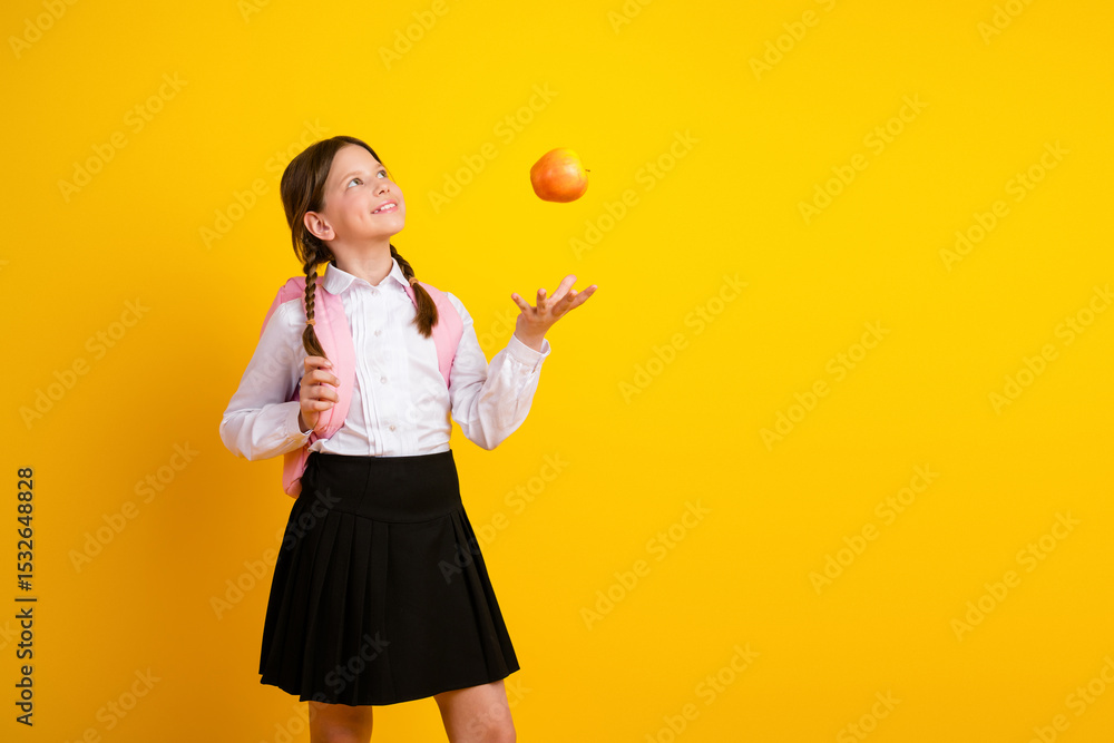 Happy schoolgirl tossing an apple against a bright yellow background, showcasing school spirit and academic enthusiasm. Happy schoolgirl tossing an apple against a bright yellow background, showcasing school spirit and academic enthusiasm.