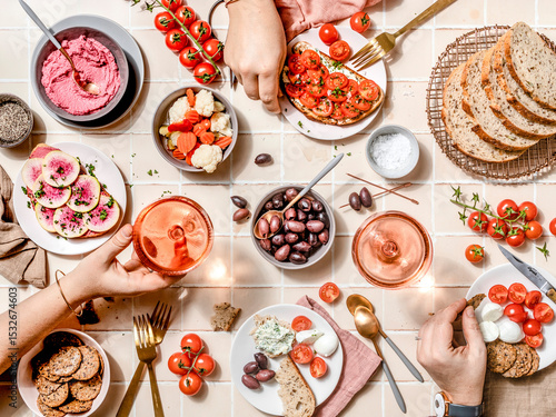 Overhead shot of women hands sharing a colorful Mediterranean brunch with fresh vegetables, bread, and drinks on a tiled table.jpg