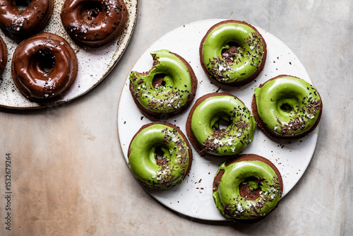 An assortment of chocolate and matcha glazed donuts on ceramic plates.