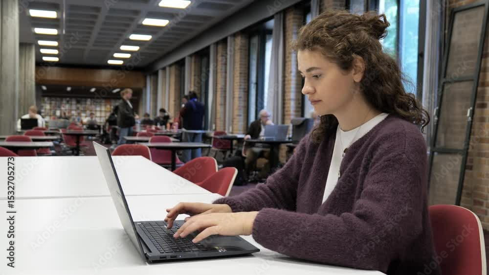 Student studies diligently in library with laptop during quiet afternoon hours Student studies diligently in library with laptop during quiet afternoon hours