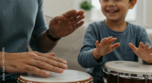A man and a young child are playing hand drums indoors, both smiling and enjoying the musical activity together in a casual setting.