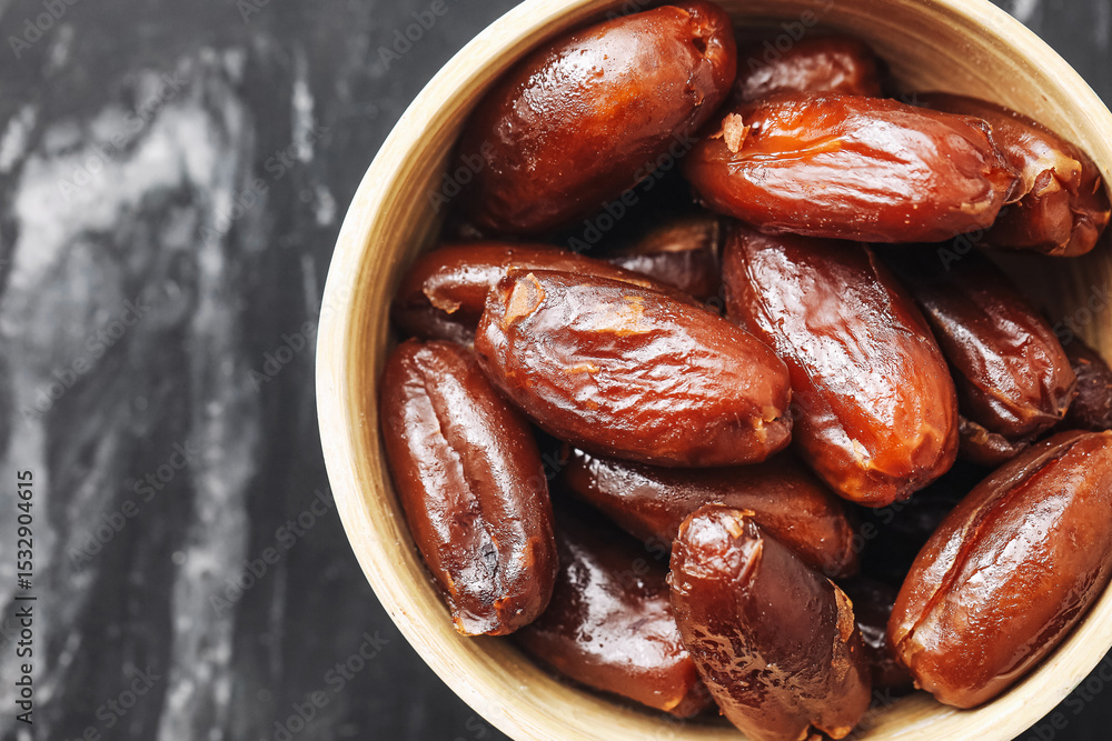 Obraz premium Natural dried dates in black bowl. Sweet brown exotic fruit closeup. Organic healthy snack rich in fiber. Traditional Ramadan food. Tasty dessert ingredient. Rustic kitchen marble background.
