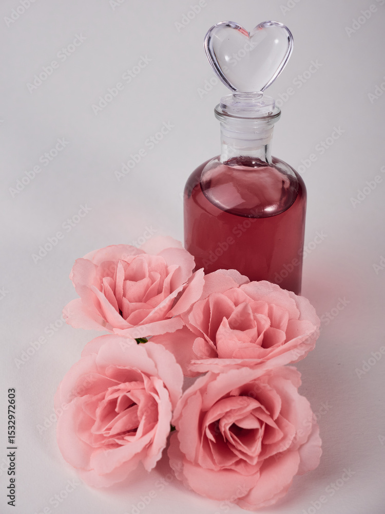 Vertical shot of a glass bottle of love potion and pink roses Vertical shot of a glass bottle of love potion and pink roses