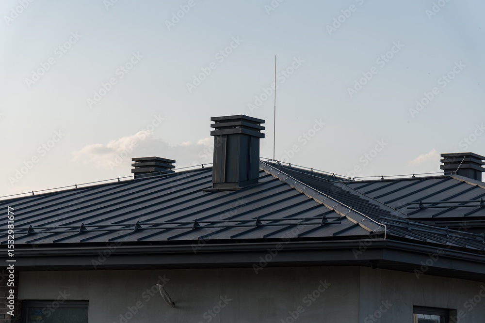 Fototapeta premium A contemporary house rooftop features sleek metal chimneys and angled panels, set against a bright sky during daytime hours
