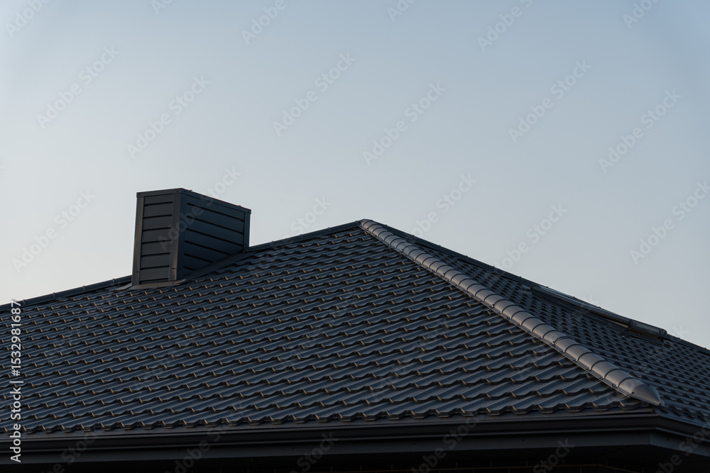 A modern house features a gray tiled roof with a prominent chimney, set against a clear blue sky during the day A modern house features a gray tiled roof with a prominent chimney, set against a clear blue sky during the day