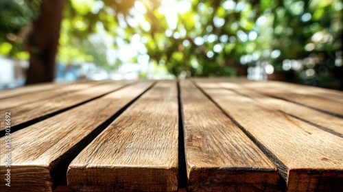 Fototapeta Naklejka Na Ścianę i Meble -  Close-up view of wooden planks on a rustic outdoor table with blurred green foliage background