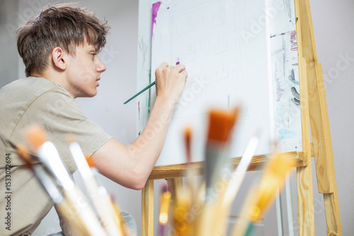 Fototapet artist at work, teenage boy sitting at an easel and learning to draw with a penc