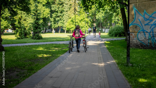 Wallpaper Mural Woman cyclist walking with leading two bicycles in the park ready for getting on with some sport exercises Torontodigital.ca