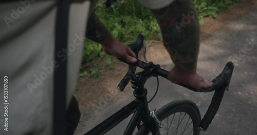 Close-up of tattooed hands gripping the handlebars of a moving black bicycle. A shaky handheld shot adds presence and realism to this scene of freedom in nature. High quality 4k footage