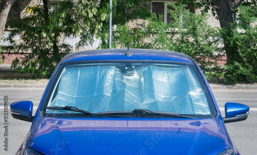 Blue car parked on the street with sunshade in windshield on a sunny day in an urban area