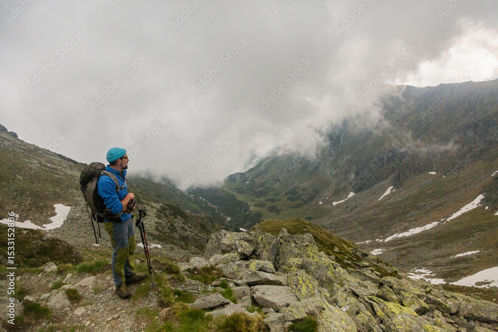 Fototapeta premium Adventure enthusiast hiking through dramatic rocky wilderness, using poles for stability while crossing steep terrain dotted with massive stones