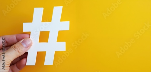 Hand holding large white hashtag sign on yellow background. Digital marketing concept. Social media symbol, content promotion, web communication, trend, marketing campaign.