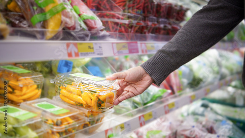Fotografi Hand picking fresh packaged yellow peppers from the vegetable shelf in modern su