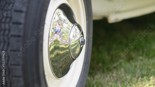 Photos Polished chrome hubcap on a vintage car whitewall wheel reflecting green lawn at an outdoor auto show