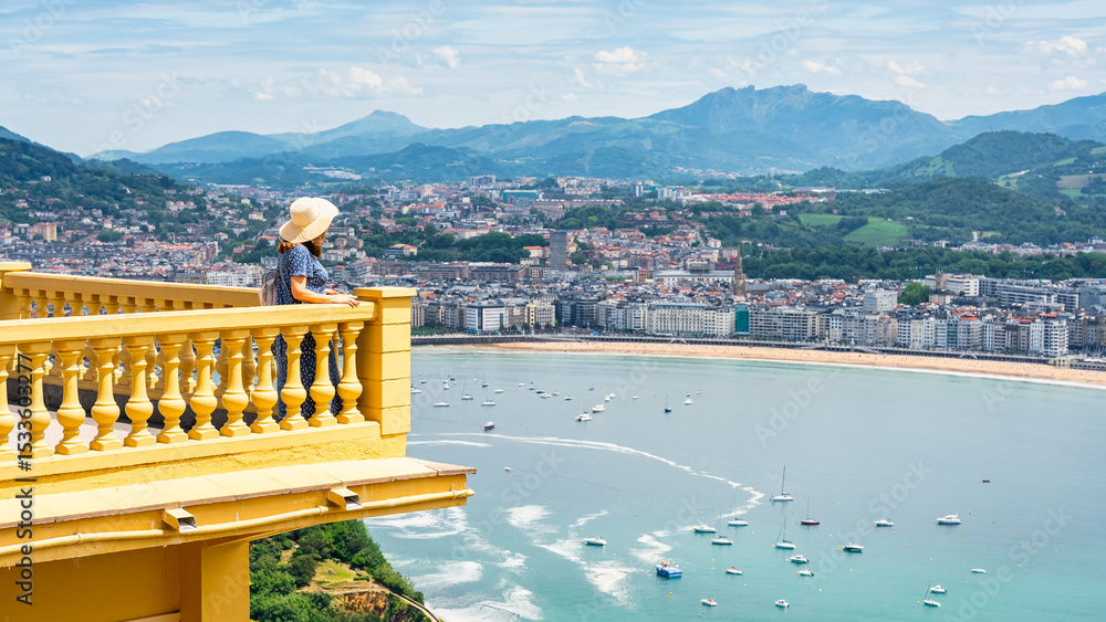 Obraz premium Tourist woman leaning out of a balcony overlooking La Concha Bay in San Sebastian, Basque Country.