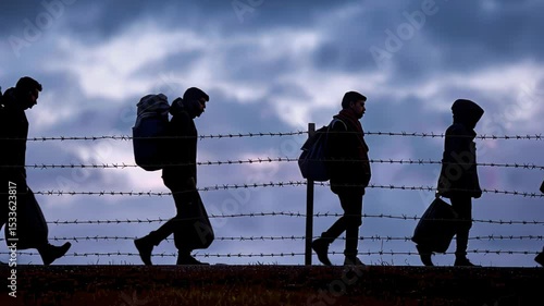 silhouettes migrants traveling along a barbed wire fence during twilight hours