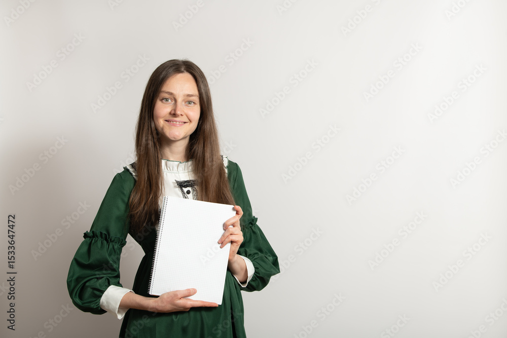 A young woman dressed in a stylish green dress stands against a light background, proudly displaying a blank notepad. She exudes confidence and creativity, perfect for artistic endeavors A young woman dressed in a stylish green dress stands against a light background, proudly displaying a blank notepad. She exudes confidence and creativity, perfect for artistic endeavors