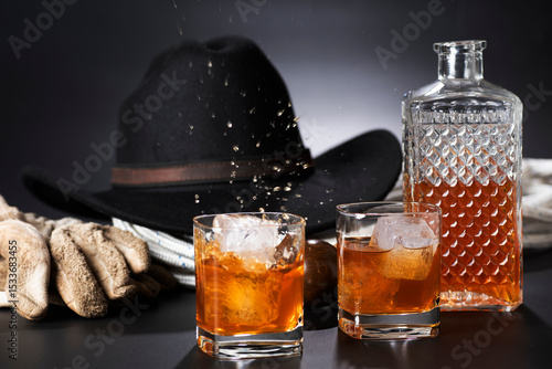 Whisky con ghiaccio su sfondo nero con cappello e guanti.