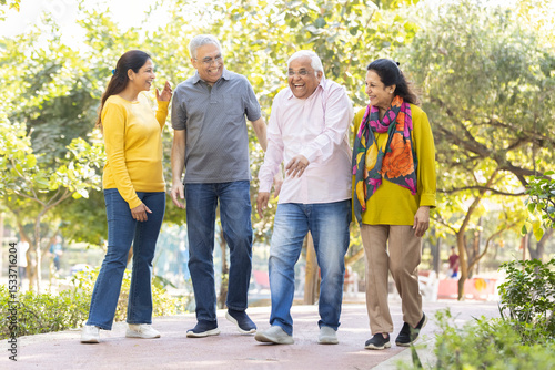 Group of happy indian senior men and women laughing and walking together in summer park. Retirement life, retired people enjoying in garden