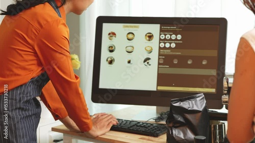 A young Asian female barista in modern cafe assists woman customer ordering latte, fresh coffee beans, dark roast, croissant, completing the purchase with mobile payment at the POS using QR code.