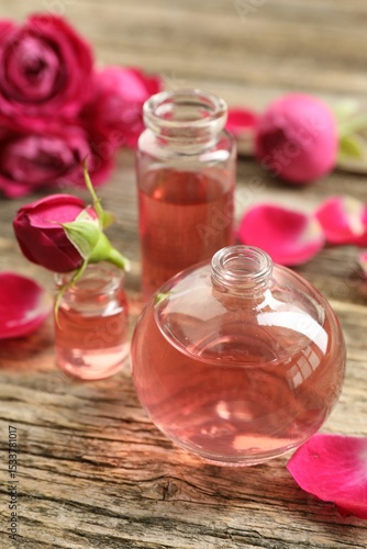 Open perfume bottles with aromatic essential oils and roses on wooden table, closeup