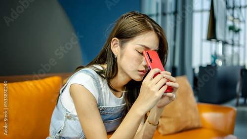 Worried young asian woman holding phone feeling jealousy anxiety waiting for mobile call sit alone at home, thoughtful stressed doubtful lady looking at smartphone thinking of cheating boyfriend
