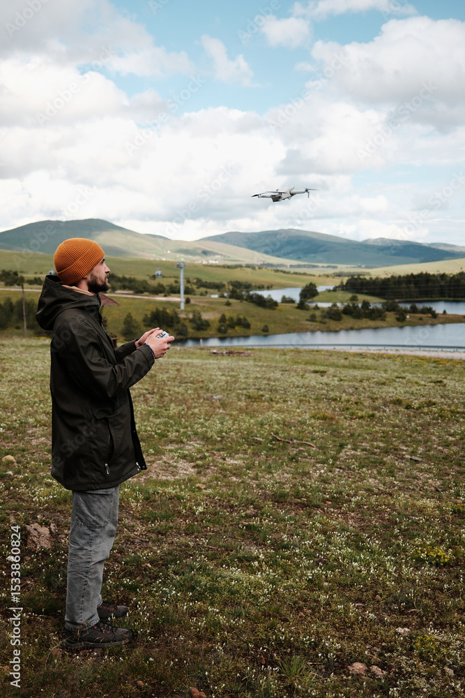 Man flying a drone above Ribnicko Lake in Zlatibor, Serbia. A scenic spring day with hills and water in the background. Travel blogger making video outdoor . Side view portrait. Man flying a drone above Ribnicko Lake in Zlatibor, Serbia. A scenic spring day with hills and water in the background. Travel blogger making video outdoor . Side view portrait.