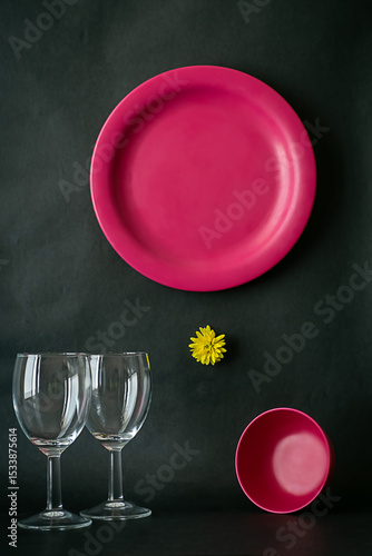 Image of a pink dinner set against dark background shot in window light. Set contains a plate, a bowl and a set of wine glasses.