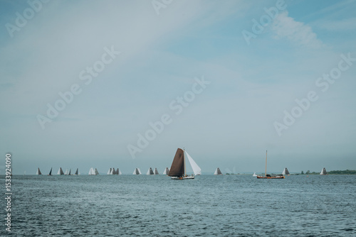 Auf dem IJsselmeer zieht sich eine eindrucksvolle Regatta von Plattbodenschiffen in breitem Panorama über das Wasser, ihre braunen und weißen Segel blähen sich im Wind.