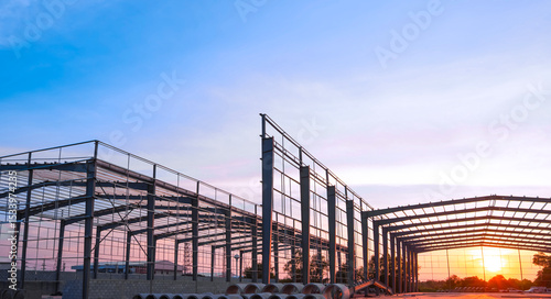 Silhouette steel structure of modern industrial factory building in construction site against sunset sky background, low angle view