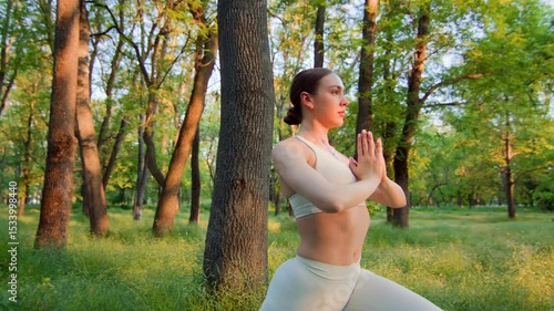 Through a series of standing yoga poses, a woman in white activewear transitions gracefully in sunset forest park light. Slow camera motion captures her breath, control, and grounded presence.