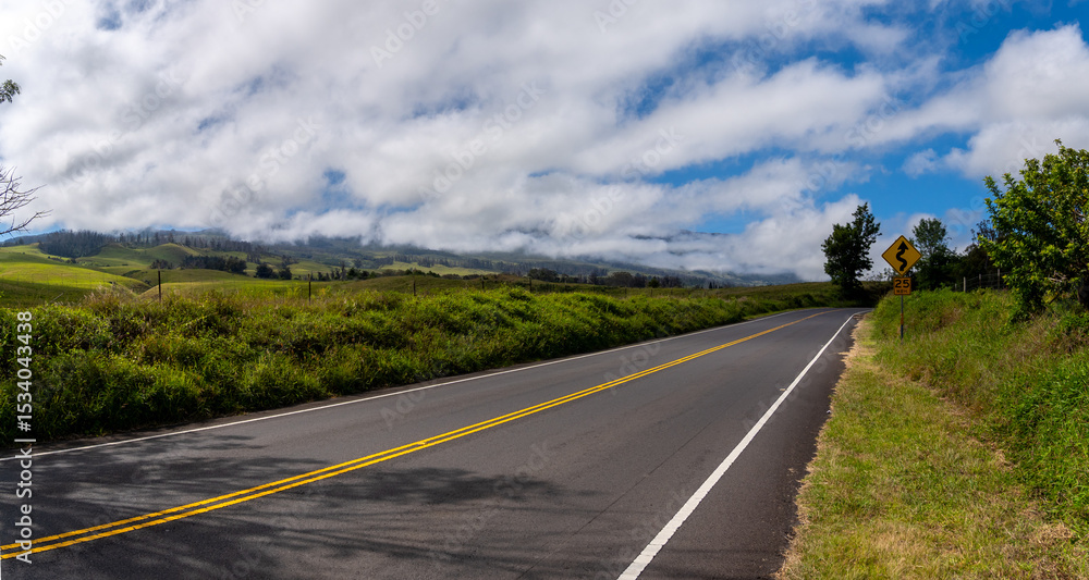 Scenic road winds through green hills under a cloudy sky, speed limit sign visible. Scenic road winds through green hills under a cloudy sky, speed limit sign visible.
