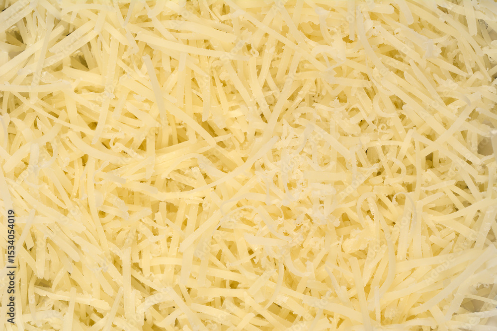 A vibrant, close-up, top-down view showcases a heap of finely grated light yellow cheese, filling the entire frame with its textured strands A vibrant, close-up, top-down view showcases a heap of finely grated light yellow cheese, filling the entire frame with its textured strands