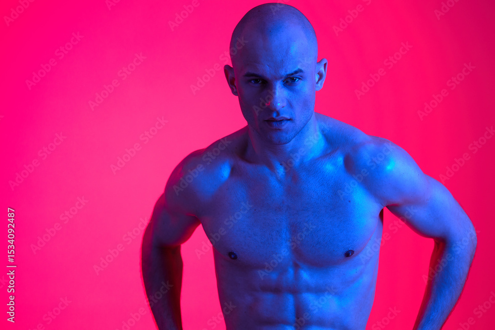 Fototapeta premium Strong man posing in vibrant blue light, showcasing athletic physique. The dramatic colors create an engaging and energetic atmosphere, highlighting his defined muscles.
