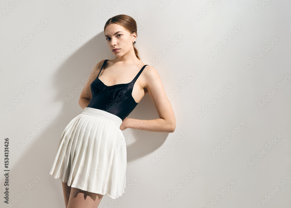 Naklejka premium A stylish woman in a tennis skirt and black bodysuit poses leaning against a wall