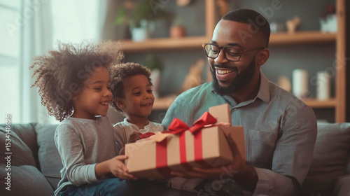 Father receives a gift from his two children while sitting on a couch in a living room setting