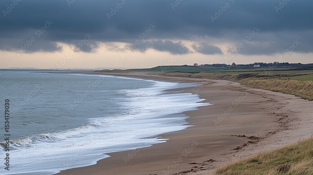 Serene coastal scene with gently rolling waves lapping a sandy shore under a dramatic, overcast sky. Distant fields and hints of buildings are visible Serene coastal scene with gently rolling waves lapping a sandy shore under a dramatic, overcast sky. Distant fields and hints of buildings are visible