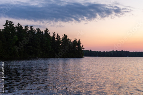 Obraz na plátně Beautiful sunrise over Lake Lovering, with blue cloud in pink sky and dark trees